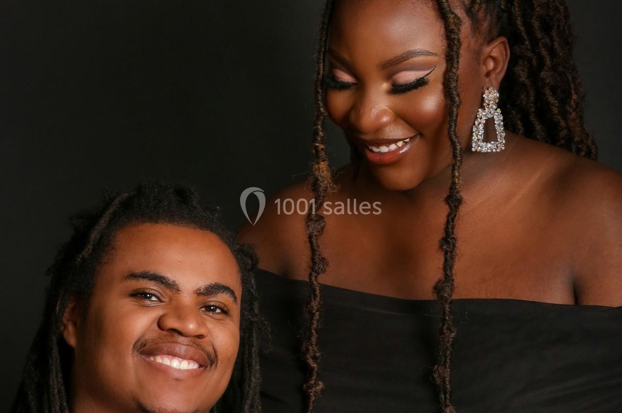 Un homme et une femme souriants, vêtus de noir, posent devant un fond sombre.