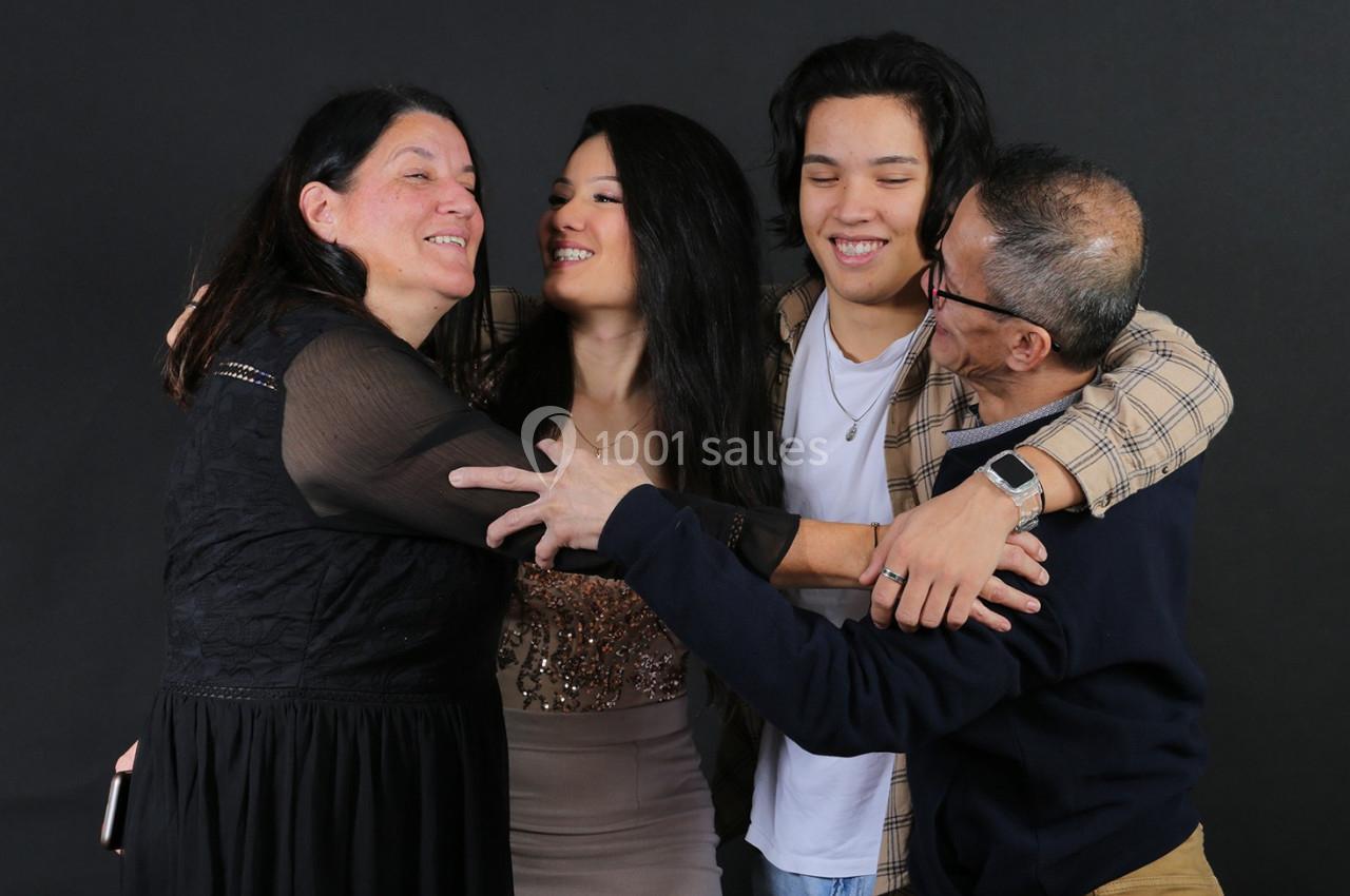 Quatre personnes souriantes s'enlaçant chaleureusement devant un fond noir.