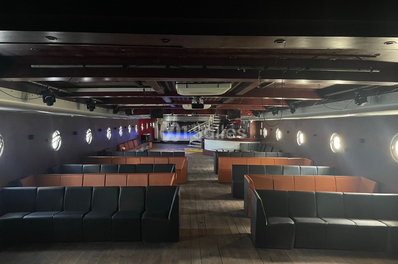 Salle intérieure avec banquettes noires et orange, scène et bar en fond, éclairage circulaire aux murs.
