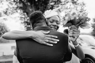 Un couple assis lors d'une cérémonie, l'homme ému essuie une larme tandis que la femme le regarde avec tendresse.