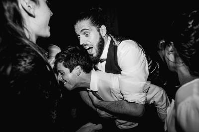 Un couple assis lors d'une cérémonie, l'homme ému essuie une larme tandis que la femme le regarde avec tendresse.