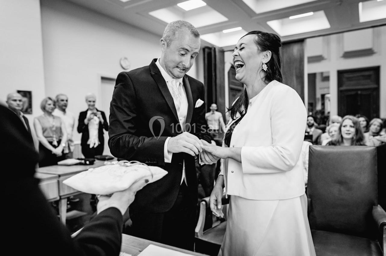 Un couple échange des alliances lors d'une cérémonie de mariage en présence d'invités dans une salle officielle.