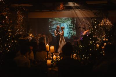 Un couple assis lors d'une cérémonie, l'homme ému essuie une larme tandis que la femme le regarde avec tendresse.