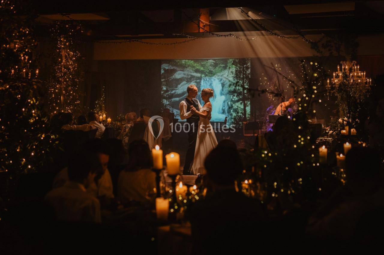 Un couple danse sous un éclairage tamisé dans une salle décorée de bougies et de guirlandes lumineuses.