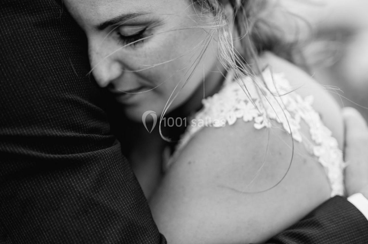 Une femme en robe blanche enlace une personne en costume, exprimant tendresse et émotion.