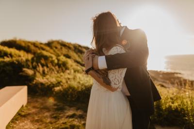 Un couple assis lors d'une cérémonie, l'homme ému essuie une larme tandis que la femme le regarde avec tendresse.