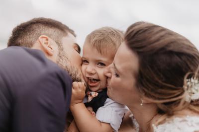Un couple assis lors d'une cérémonie, l'homme ému essuie une larme tandis que la femme le regarde avec tendresse.