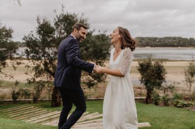 Un couple assis lors d'une cérémonie, l'homme ému essuie une larme tandis que la femme le regarde avec tendresse.
