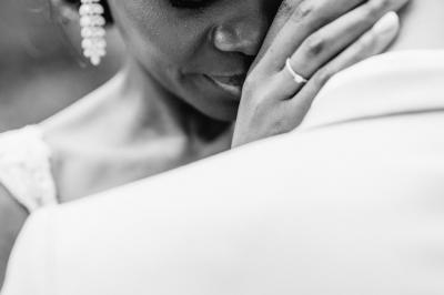 Un couple assis lors d'une cérémonie, l'homme ému essuie une larme tandis que la femme le regarde avec tendresse.