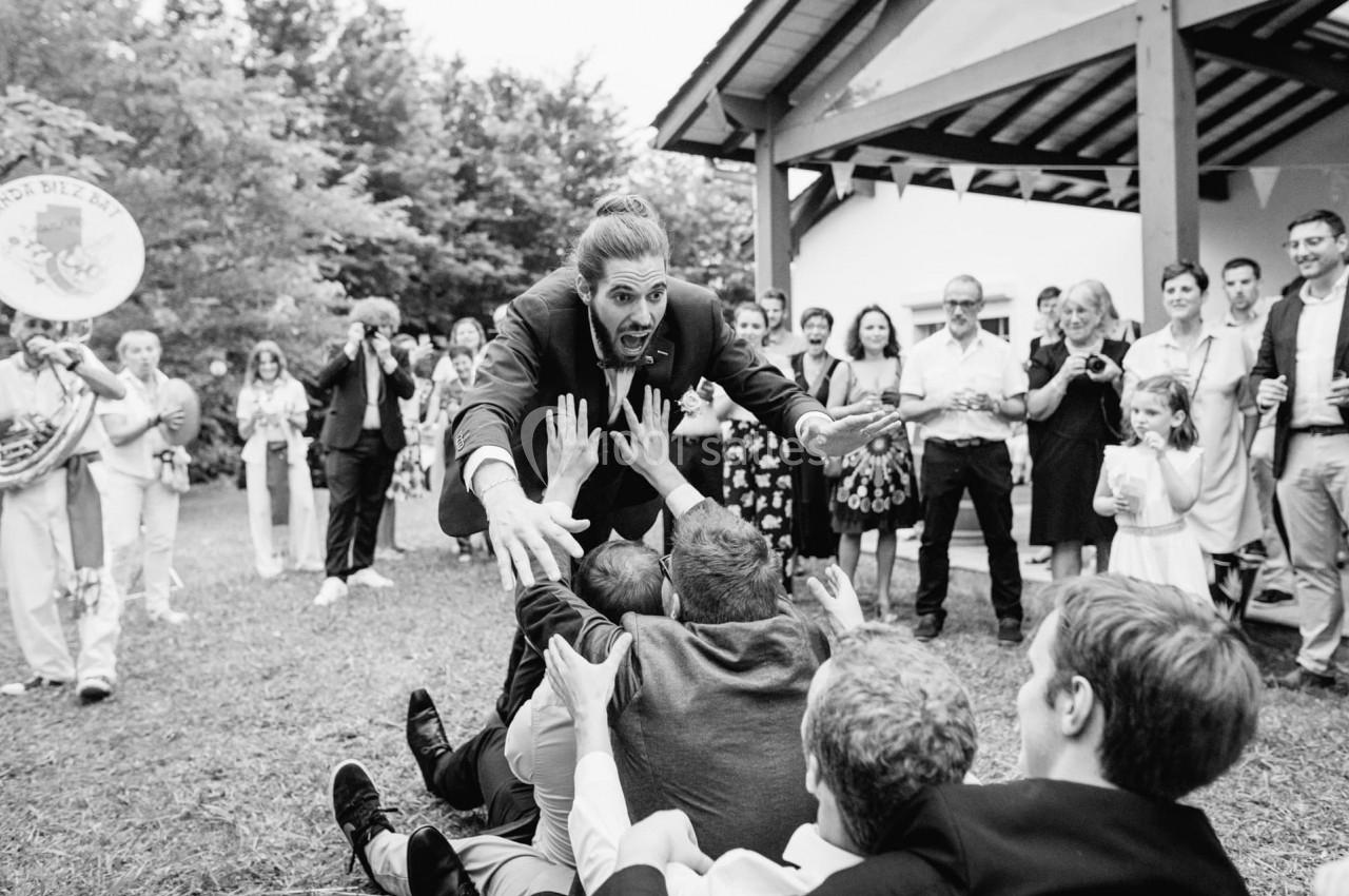 Un homme en costume s'approche de personnes assises au sol lors d'un événement en extérieur, entouré de spectateurs.