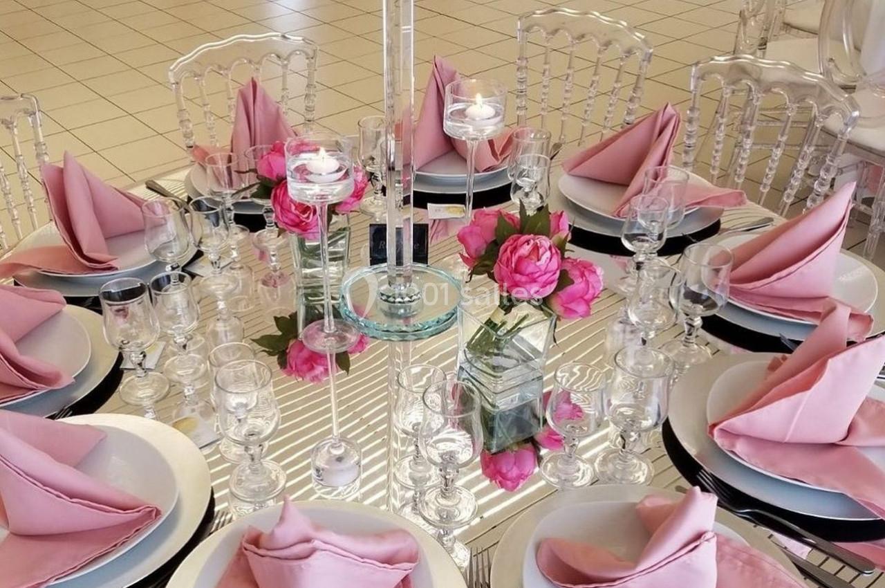 Table ronde élégamment dressée avec des serviettes roses pliées, des verres, des assiettes et un vase de fleurs roses au…