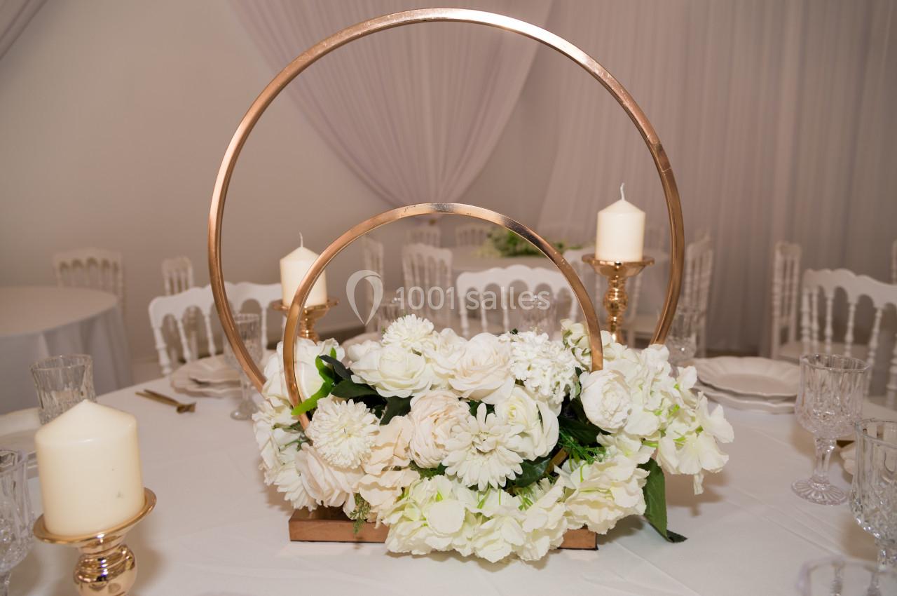 Centre de table avec des fleurs blanches, des bougies et des cercles dorés sur une nappe blanche.