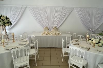 Salle de réception décorée avec des tables rondes, des chaises blanches, des chandeliers et des drapés blancs au plafond.