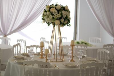 Salle de réception décorée avec des tables rondes, des chaises blanches, des chandeliers et des drapés blancs au plafond.