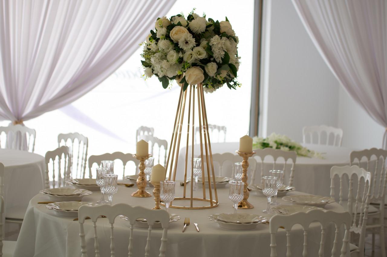 Centre de table floral avec roses blanches sur un support doré, entouré de bougies et vaisselle élégante.