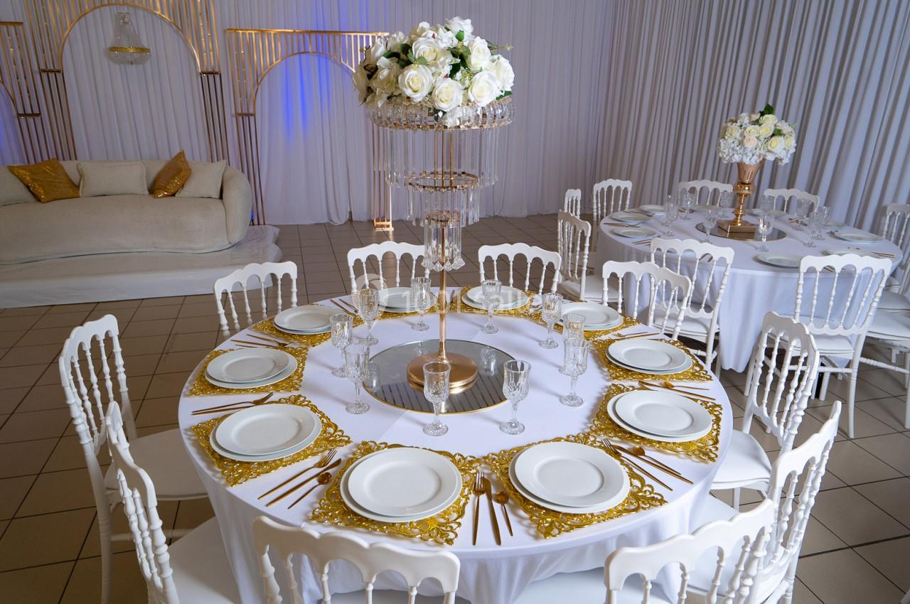 Table ronde élégamment dressée avec des assiettes blanches, des couverts dorés et un centre de table floral.