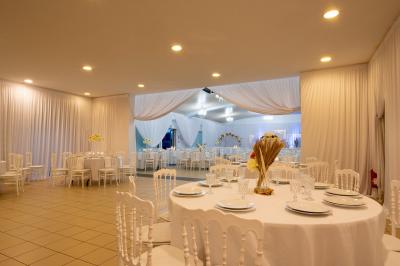 Salle de réception décorée avec des tables rondes, des chaises blanches, des chandeliers et des drapés blancs au plafond.