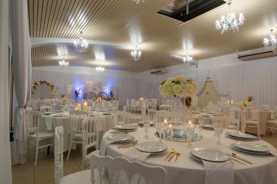 Salle de réception décorée avec des tables rondes, des chaises blanches, des chandeliers et des drapés blancs au plafond.