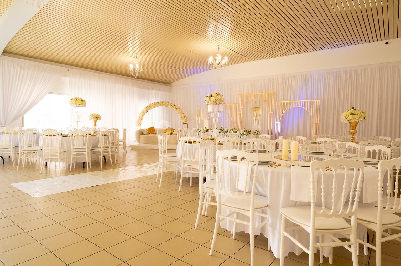 Salle de réception décorée avec des tables rondes, des chaises blanches et des arrangements floraux élégants.