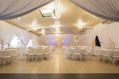 Salle de réception décorée avec des tables rondes, des chaises blanches, des chandeliers et des drapés blancs au plafond.