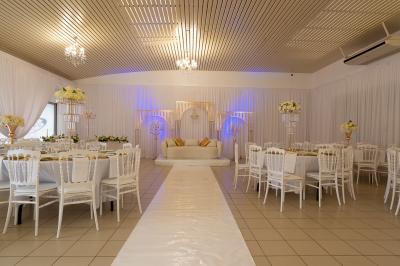 Salle de réception décorée avec des tables rondes, des chaises blanches, des chandeliers et des drapés blancs au plafond.