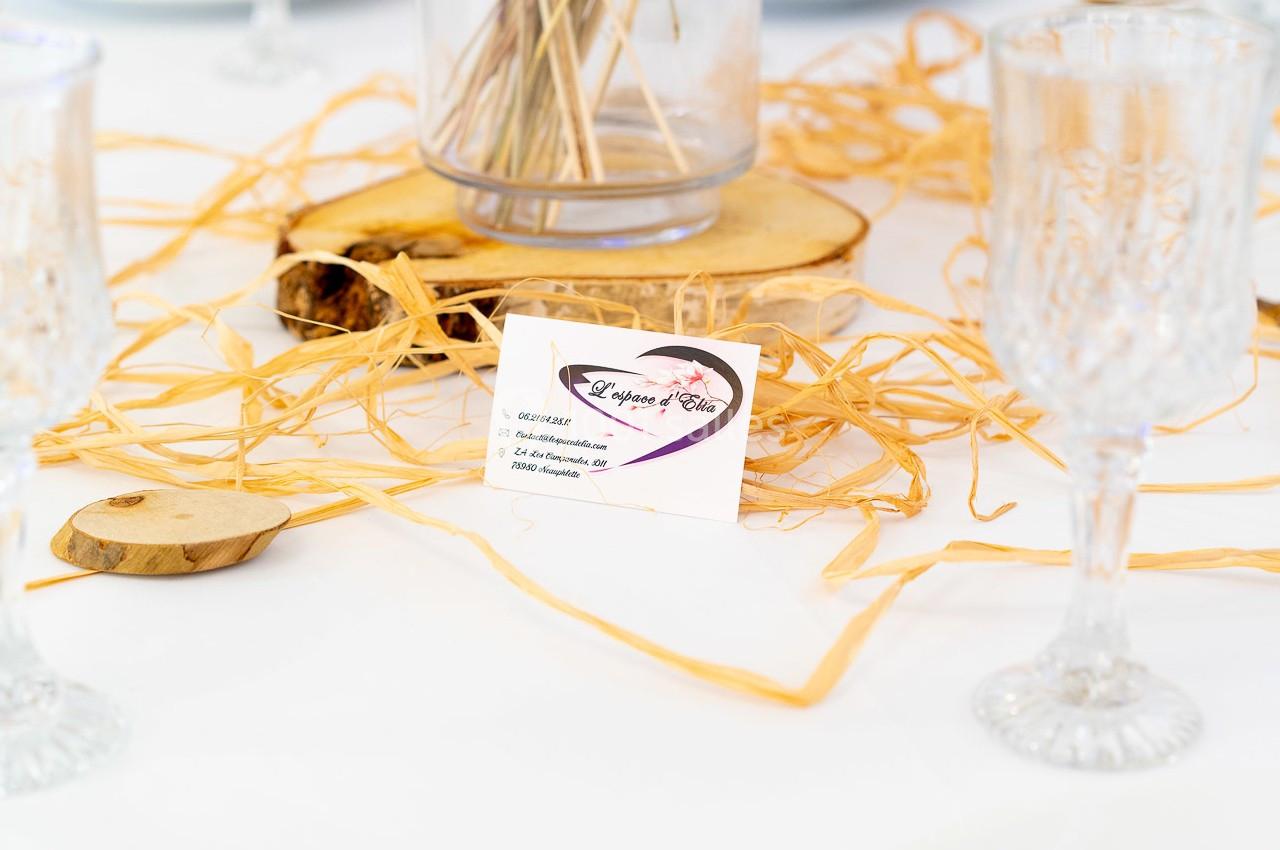 Carte de visite posée sur une table décorée de raphia, bois et verres en cristal.