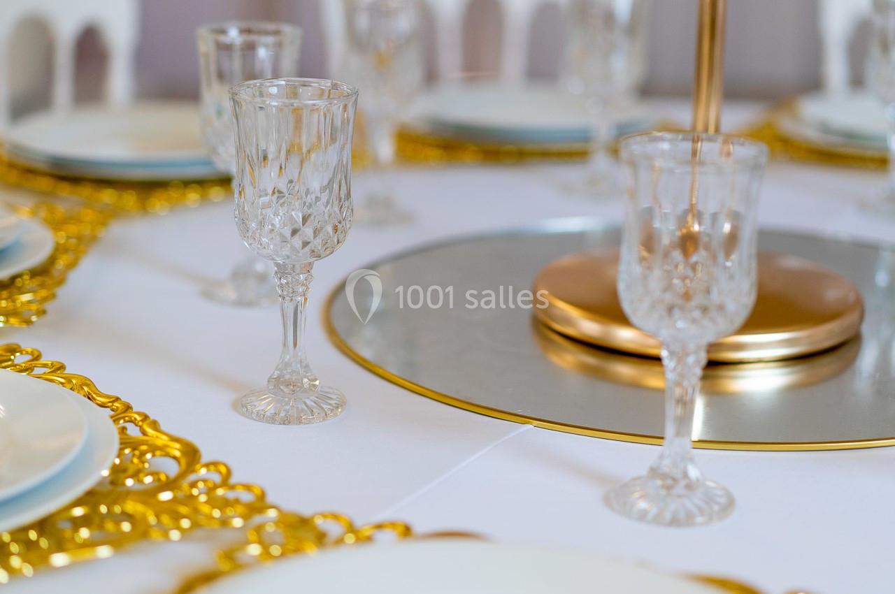 Table dressée avec des verres en cristal, assiettes blanches et détails dorés sur un centre de table élégant.