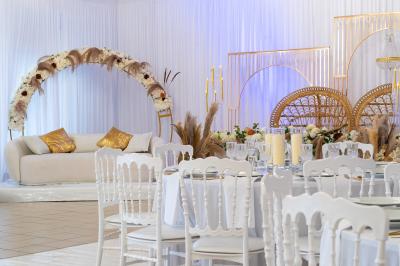 Salle de réception décorée avec des tables rondes, des chaises blanches, des chandeliers et des drapés blancs au plafond.