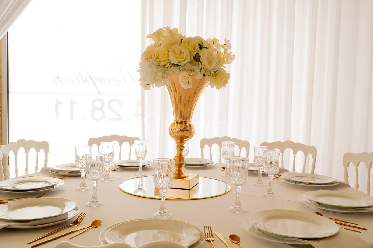 Table élégamment dressée avec vaisselle blanche, couverts dorés et un centre de table floral dans un vase doré.