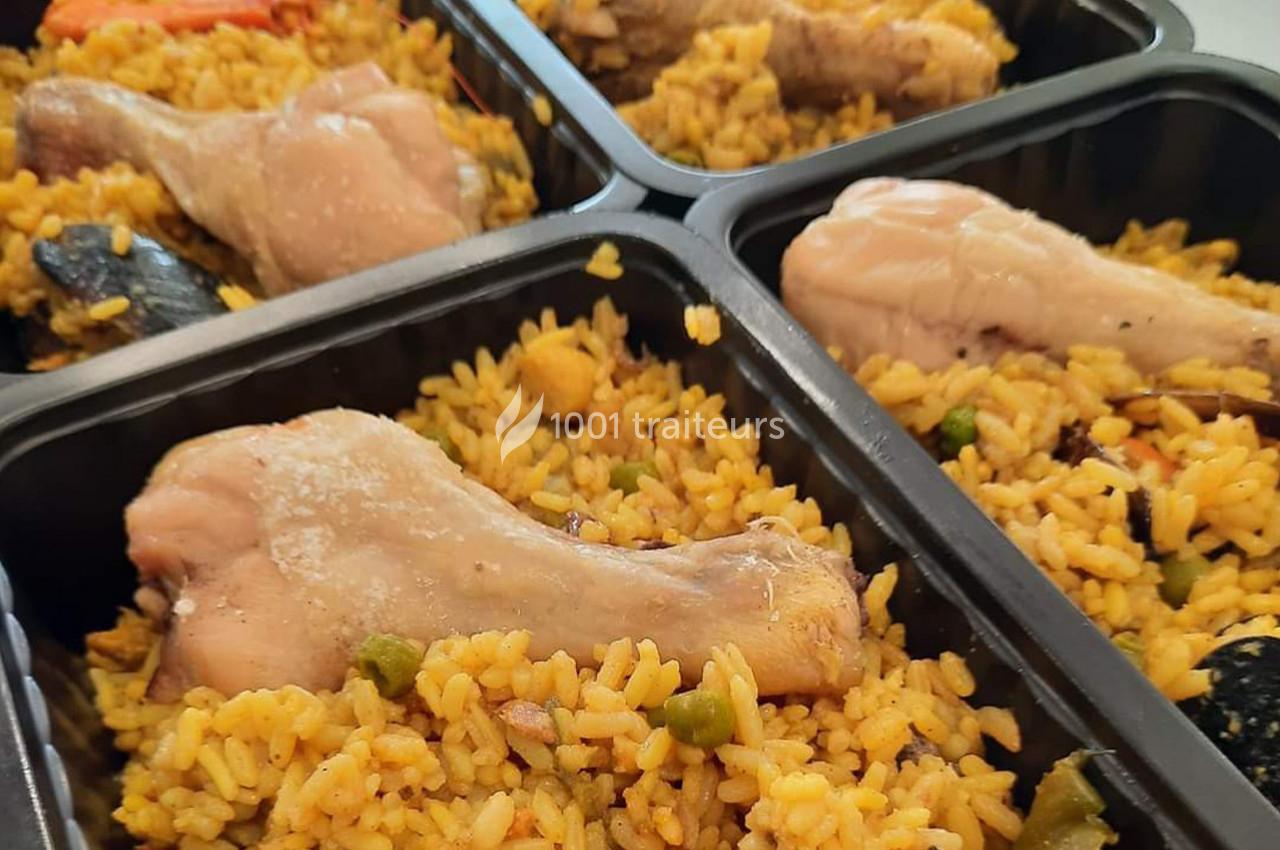 Portions individuelles de riz jaune garnies de pilons de poulet, légumes et fruits de mer dans des barquettes noires.