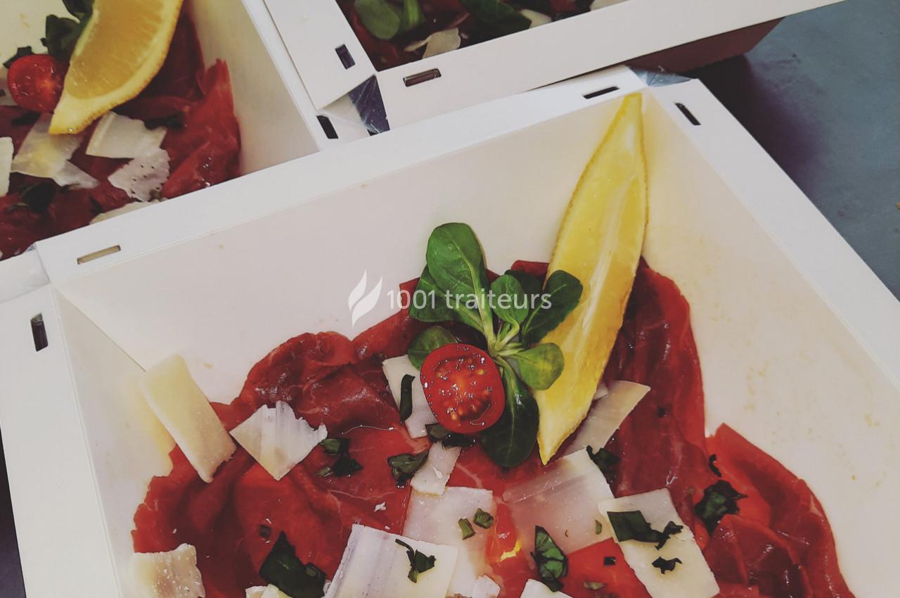 Tranches de carpaccio de bœuf garnies de parmesan, roquette, tomate cerise et citron dans des assiettes blanches.