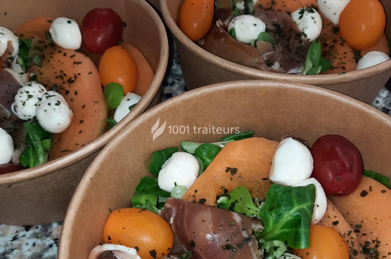 Salades composées dans des bols en carton, avec mozzarella, tomates cerises, melon, jambon cru et feuilles de salade.