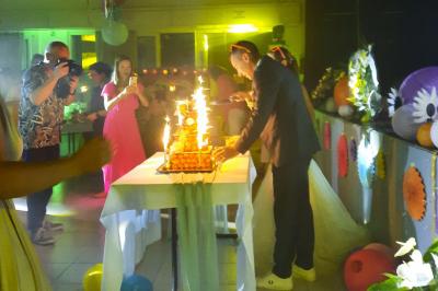 Un couple coupe un gâteau éclairé de bougies étincelantes lors d'une fête dans une salle décorée.