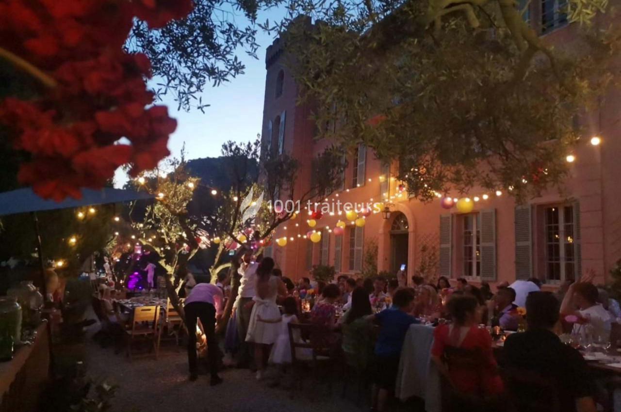 Dîner en plein air au crépuscule, avec des guirlandes lumineuses suspendues entre des arbres et des convives attablés.