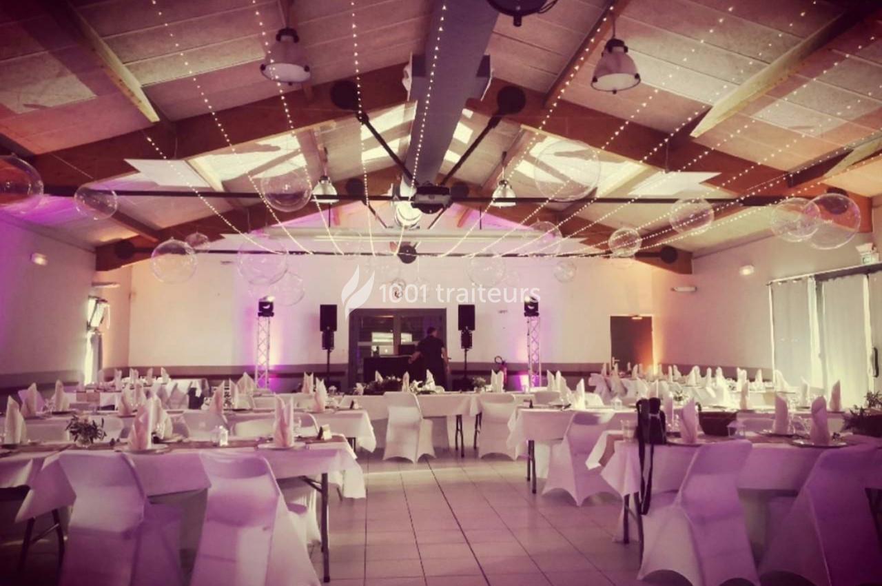 Salle de réception décorée avec des tables dressées, éclairage tamisé et guirlandes lumineuses suspendues.