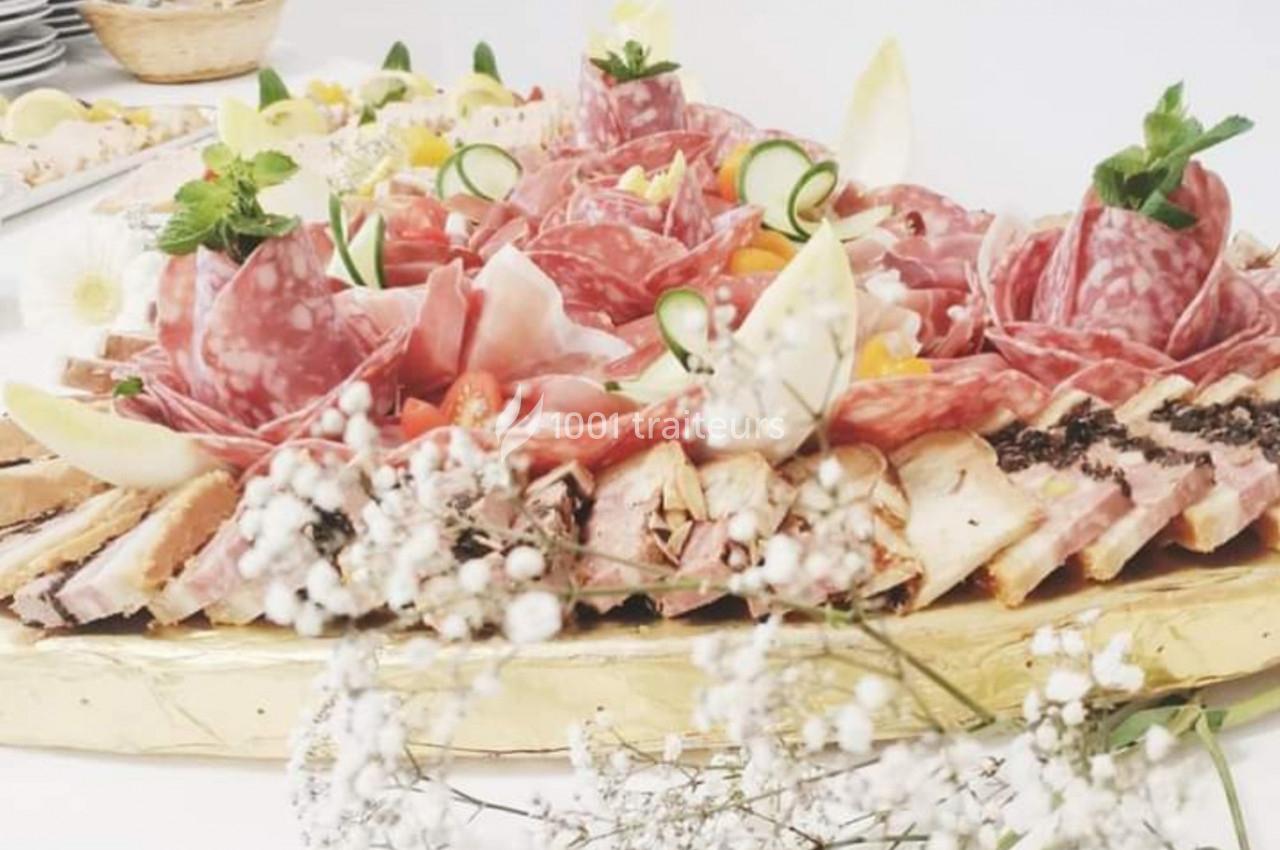 Plateau de charcuterie variée avec salami, jambon, légumes décoratifs et fleurs blanches en premier plan.