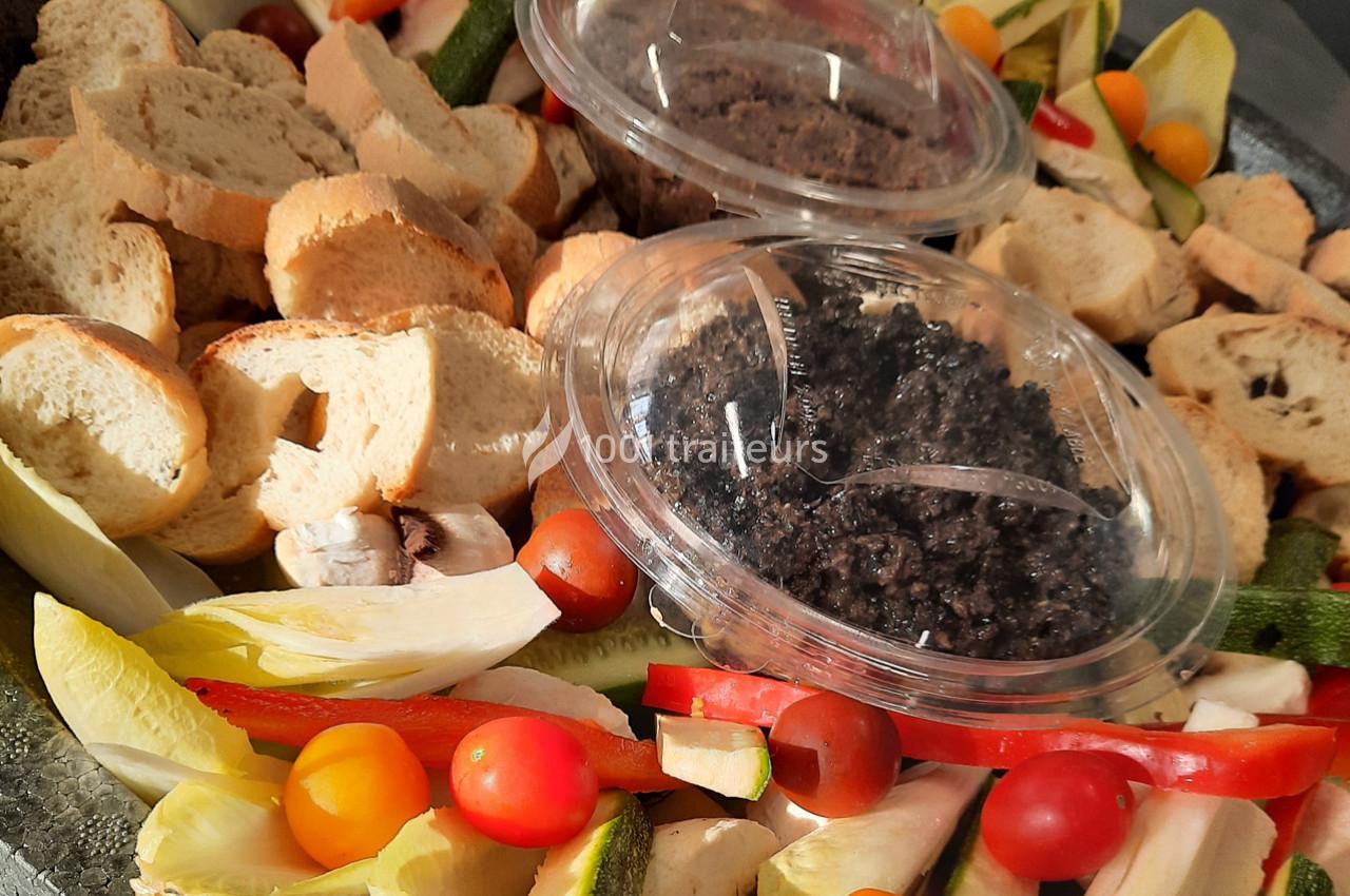 Plateau de légumes frais, tomates cerises, endives, pain tranché et tartinades dans des pots transparents.