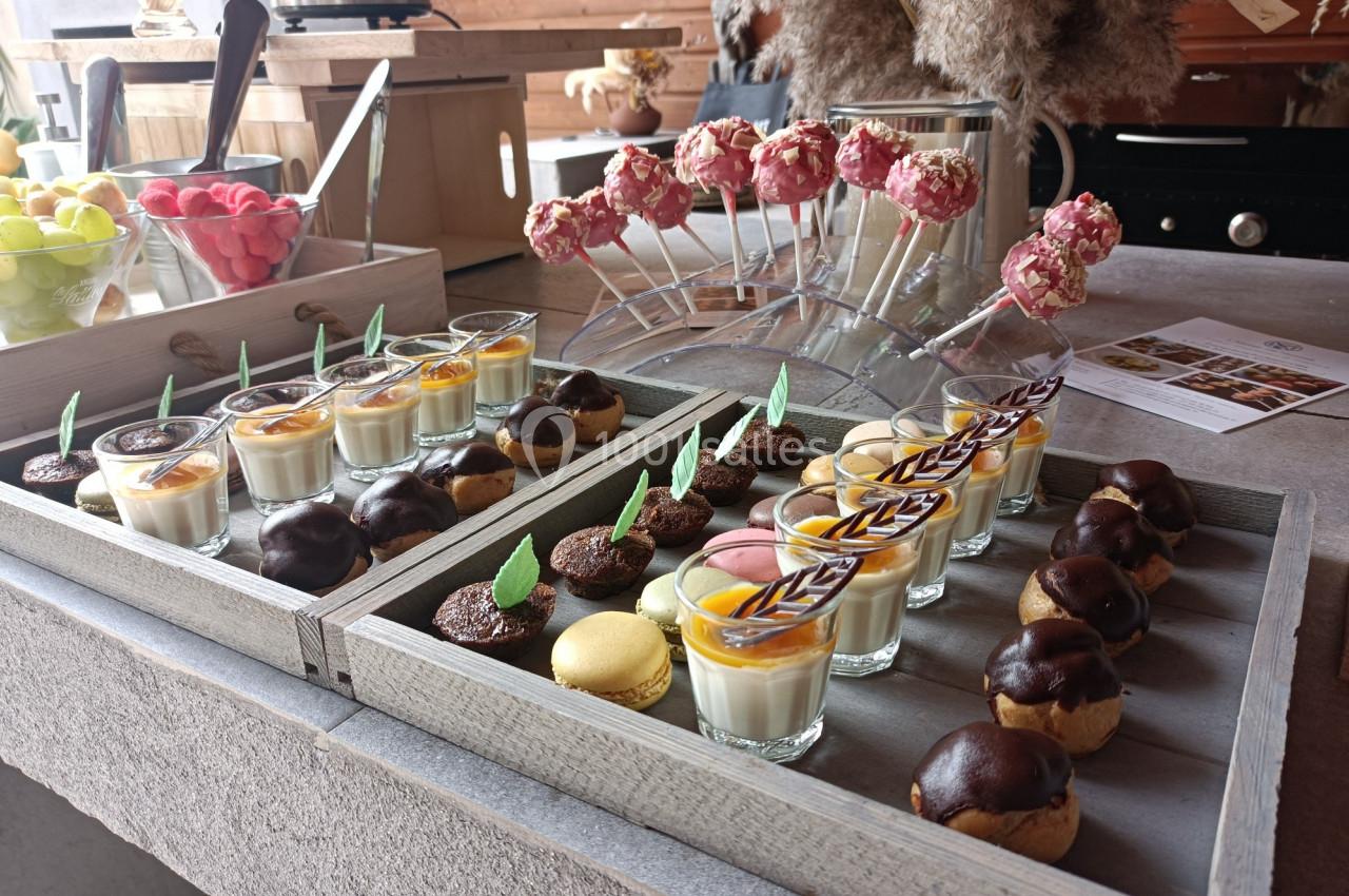 Plateau de desserts variés comprenant verrines, macarons, choux au chocolat et sucettes décorées sur une table en bois.