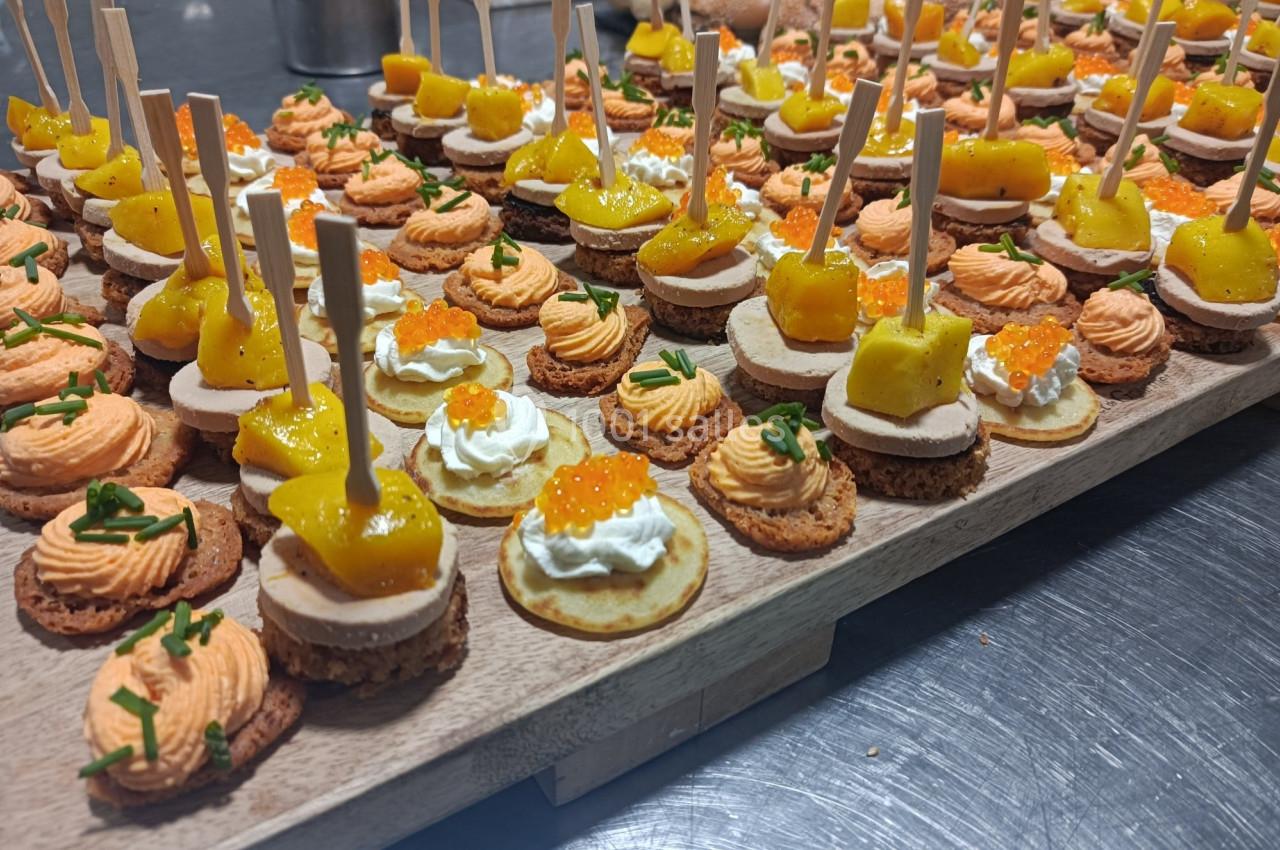 Plateau de canapés variés avec mousse, œufs de poisson, fromage et garnitures colorées sur un plan de travail.