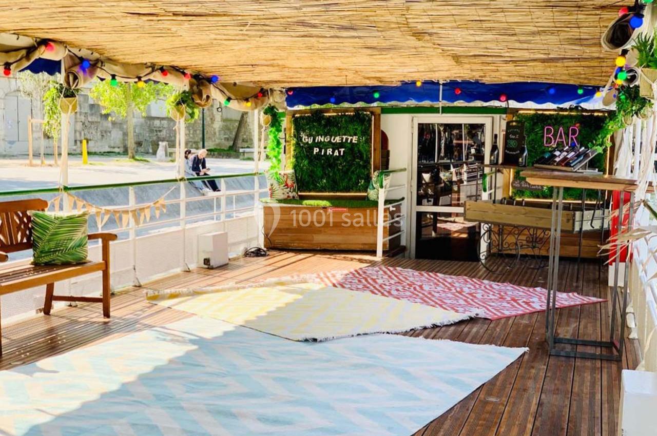 Terrasse en bois décorée avec des tapis colorés, des plantes et un bar en arrière-plan sous un toit en bambou.