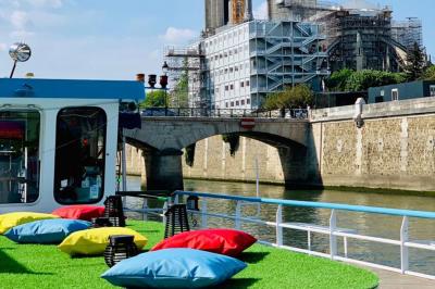 Intérieur d'une péniche aménagée avec un parquet en bois, un bar en bois, des plantes et des sièges décorés de coussins.