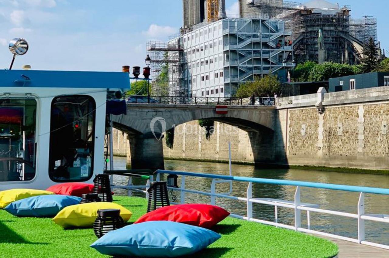 Bateau avec terrasse colorée sur la Seine, vue sur un pont et la cathédrale Notre-Dame en rénovation.