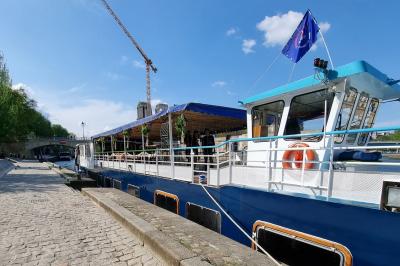 Intérieur d'une péniche aménagée avec un parquet en bois, un bar en bois, des plantes et des sièges décorés de coussins.