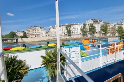 Intérieur d'une péniche aménagée avec un parquet en bois, un bar en bois, des plantes et des sièges décorés de coussins.