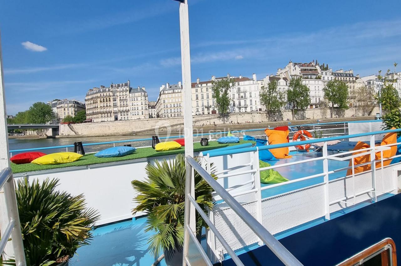 Passerelle menant à une péniche colorée avec vue sur des bâtiments historiques en bord de rivière.