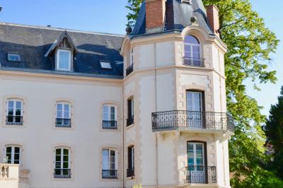 Jardin ensoleillé aménagé pour un événement avec tables hautes, tente blanche et allée décorée de fleurs.