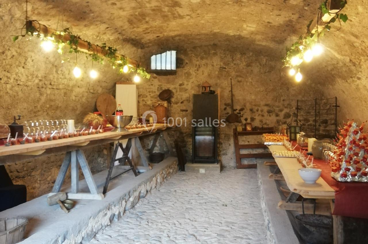 Salle voûtée en pierre aménagée avec des tables garnies de plats, boissons et décorations lumineuses.