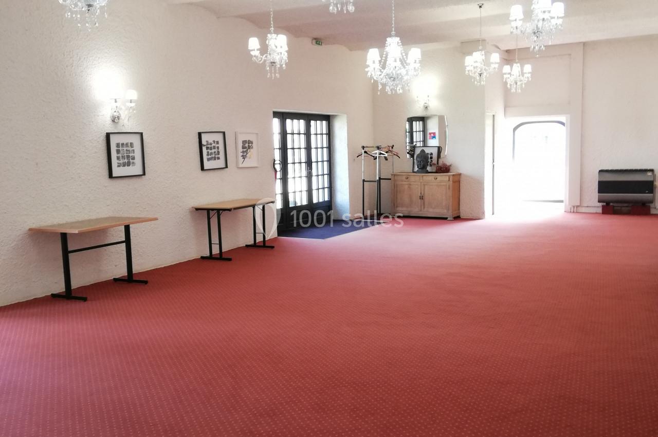 Salle spacieuse avec moquette rouge, murs blancs, lustres suspendus et mobilier minimaliste.