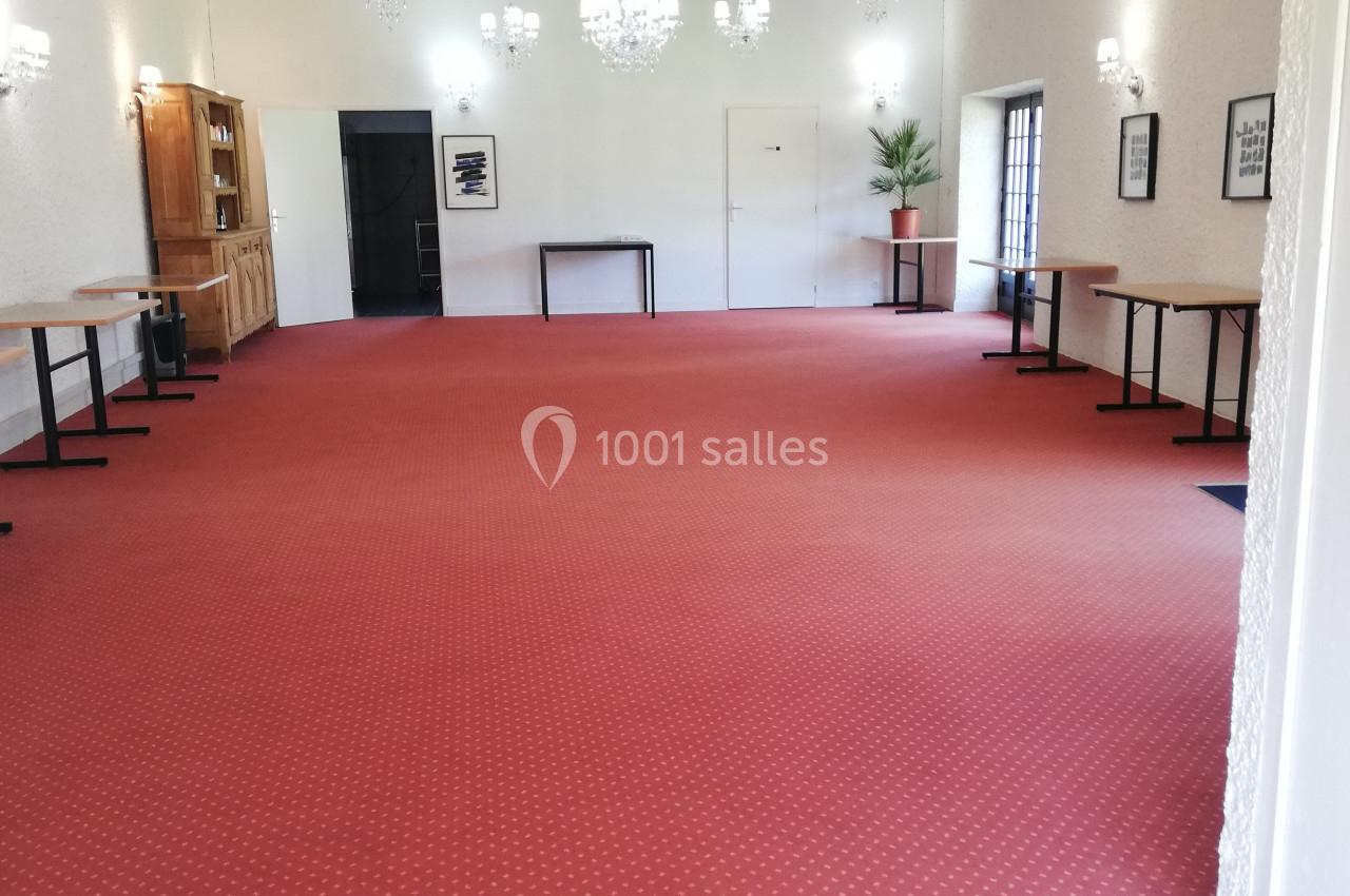 Salle spacieuse avec moquette rouge, murs blancs, lustres suspendus et tables alignées le long des côtés.
