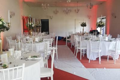 Jardin ensoleillé aménagé pour un événement avec tables hautes, tente blanche et allée décorée de fleurs.